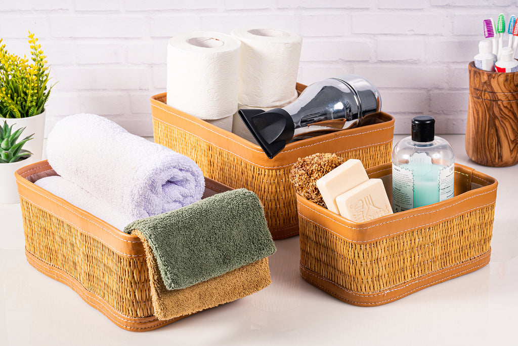 Set of 3 handmade natural fiber darido storage boxes with brown leather trim, filled with toiletries and towels. - Set of 3 Handmade Natural Fiber Storage Boxes with Colored Leather Trim