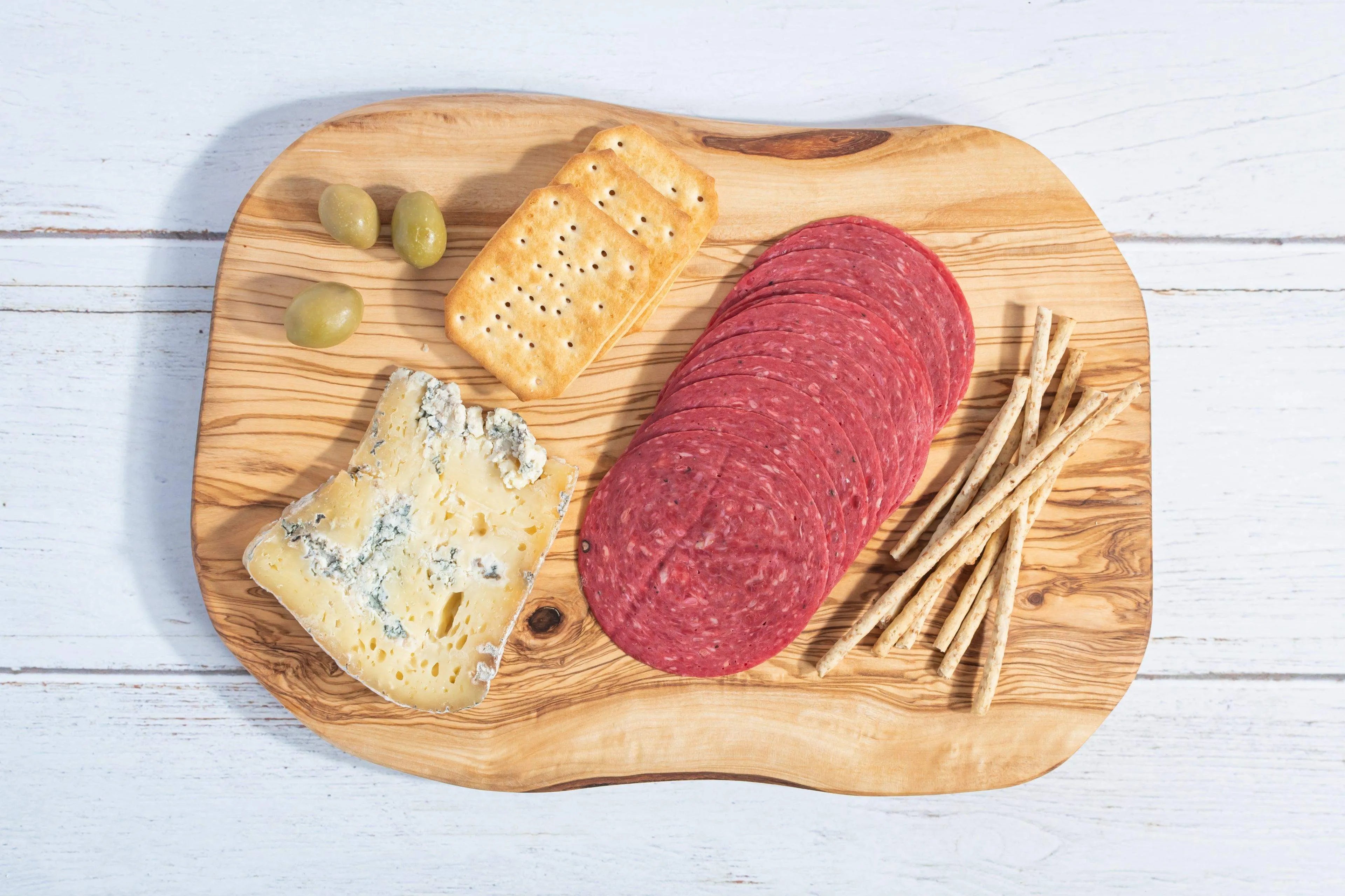 Darido handmade olive wood cutting board with cheese, salami, breadsticks, and olives on white surface. - Handmade Olive Wood Cutting Board – Reversible, Rustic & Food-Safe | 12x7" (30x18cm)