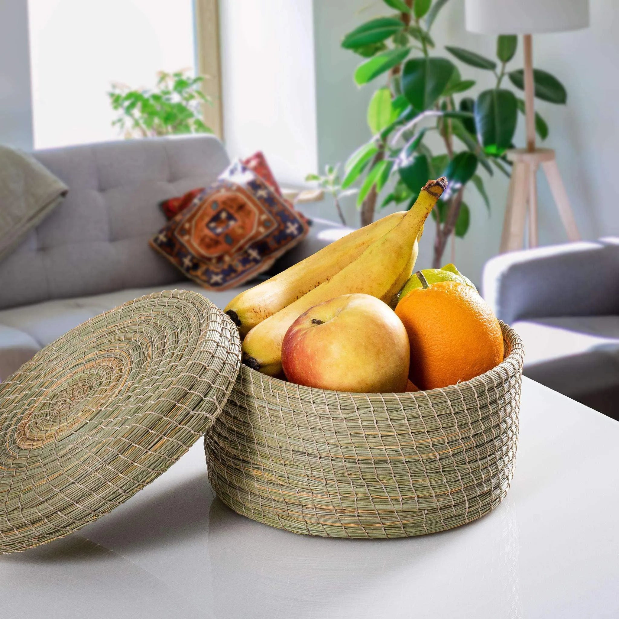 Round Darido Halfa basket with lid, natural woven texture, holding bananas, apple, and orange, on living room couch. - Round Halfa Basket