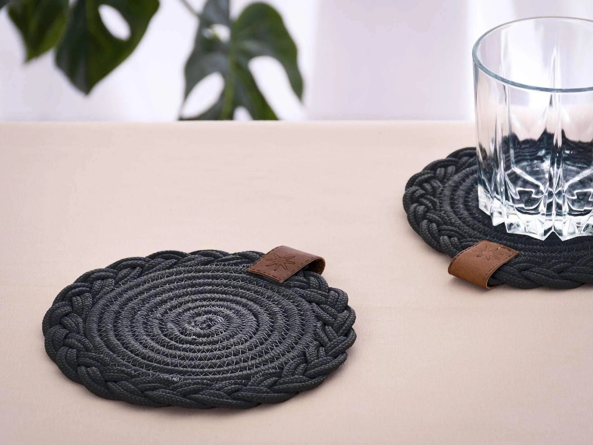 Set of 2 black Darido cotton coasters with braided design and brown leather tags, 15cm diameter. - Set of 2 Black Coasters- 15cm